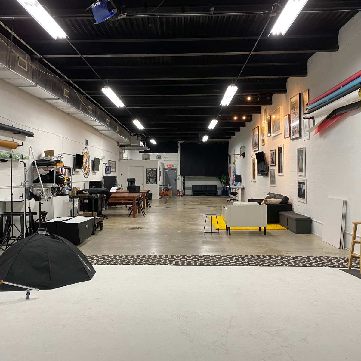 A spacious photography studio with various equipment, furniture, and a backdrop area along the walls.
