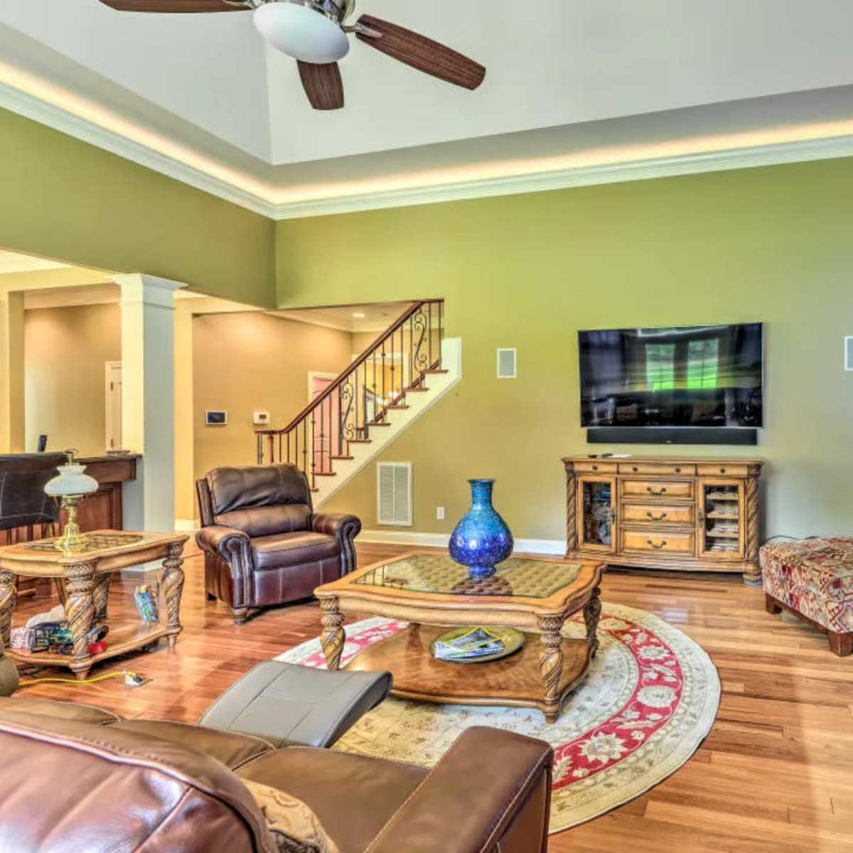The living room features a seating area with a leather recliner, a patterned sofa, a wooden coffee table, and a stone fireplace beneath a mounted television.