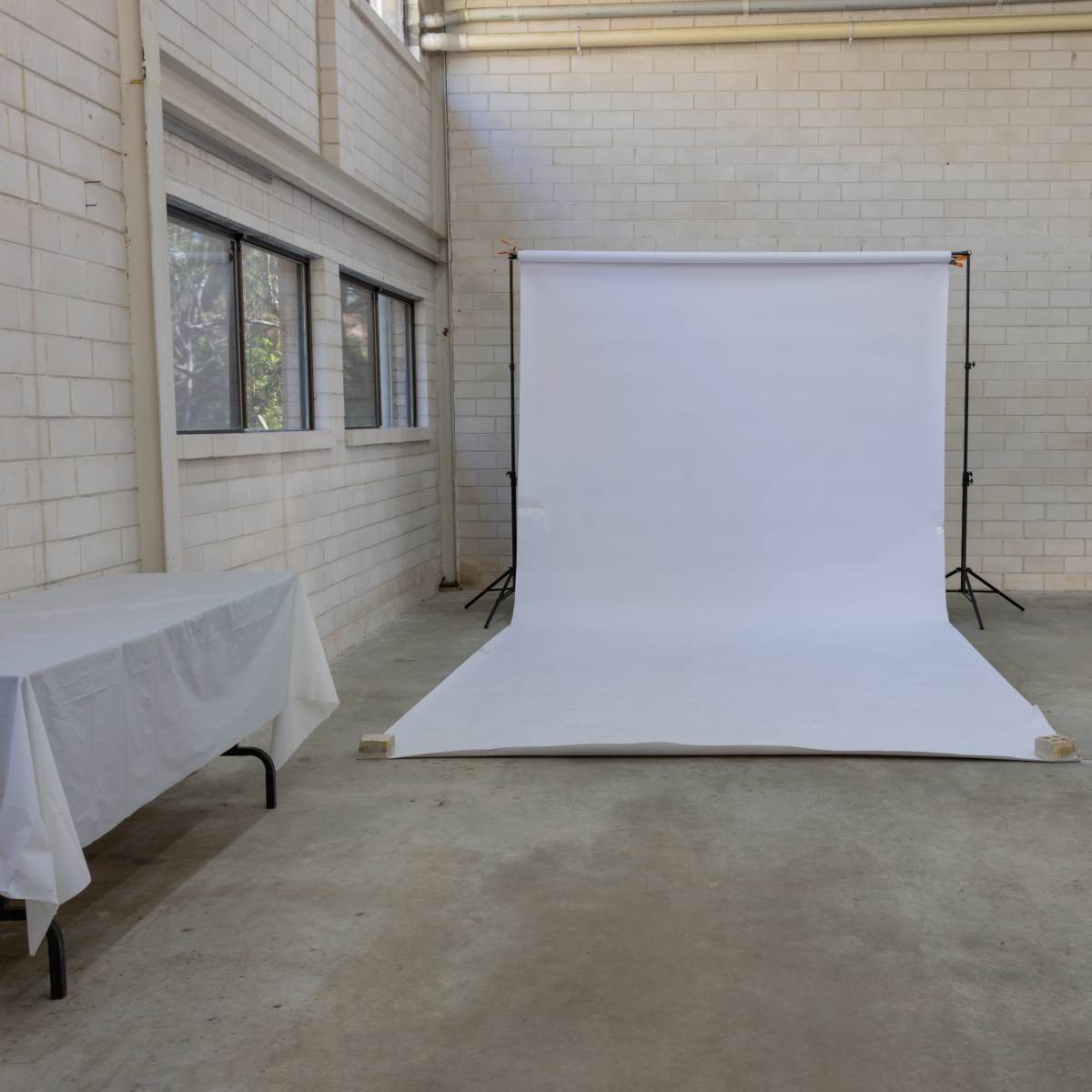 An empty studio space features a white backdrop on the floor, illuminated by natural light from large windows.