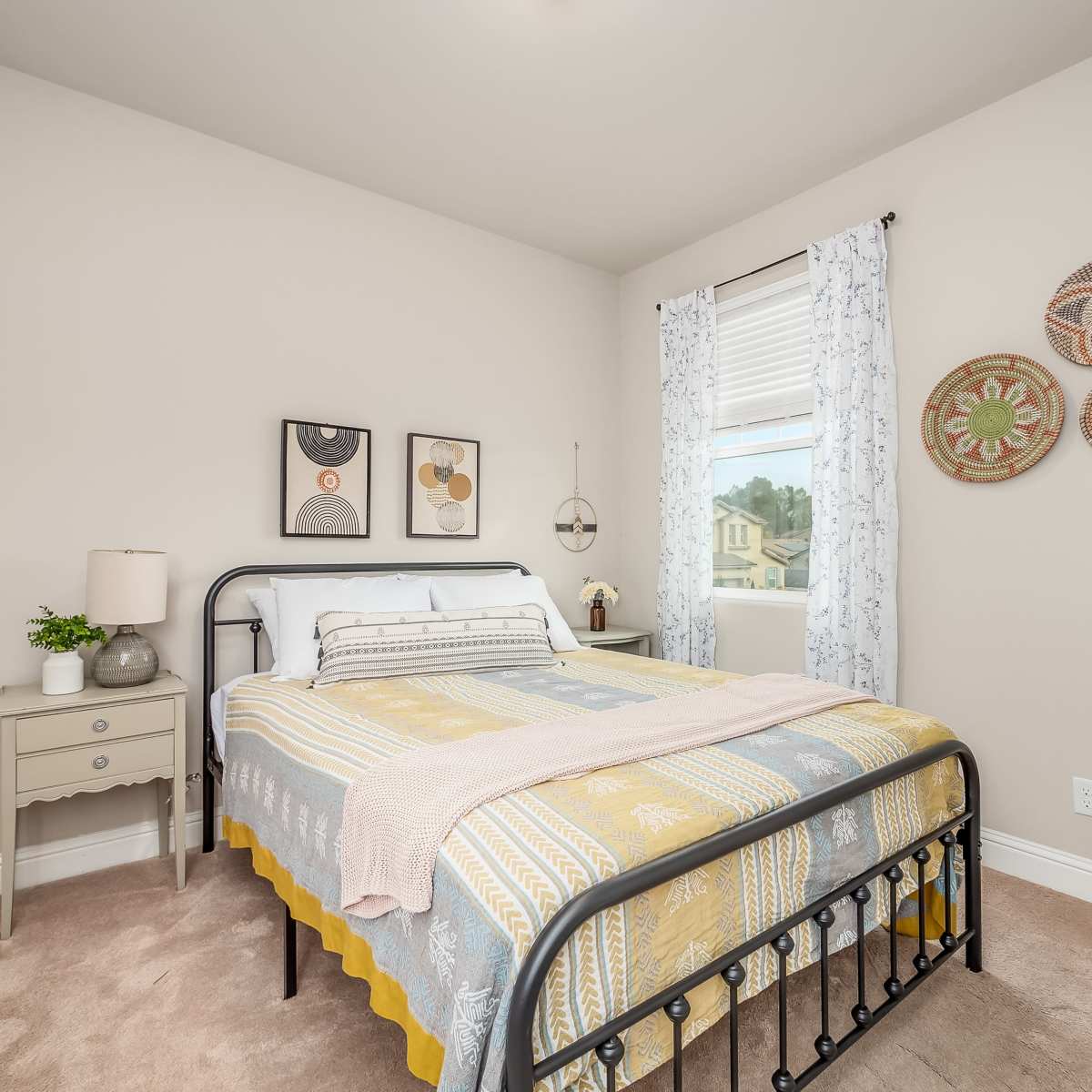 A bedroom featuring a bed with a patterned comforter, a nightstand with a lamp, and decorative wall hangings.