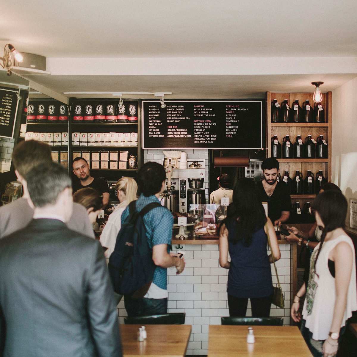 A group of customers engages with staff at a coffee shop counter while others wait in line.