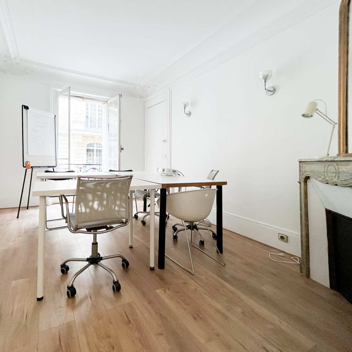 A bright, minimalist office space with a large window, a whiteboard on a stand, and two desks with chairs arranged around them.