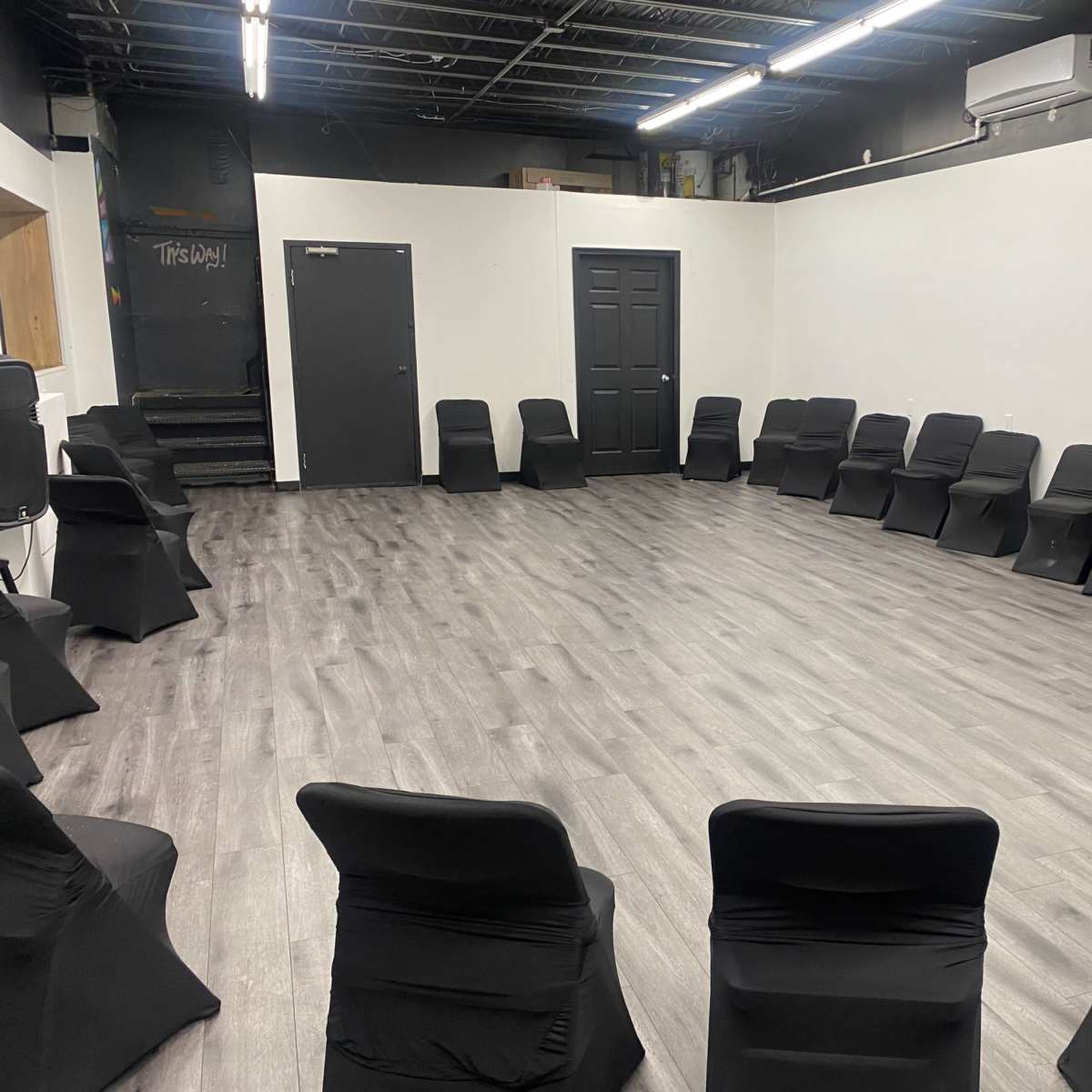A spacious room with a circle of black chairs arranged on a light wooden floor.