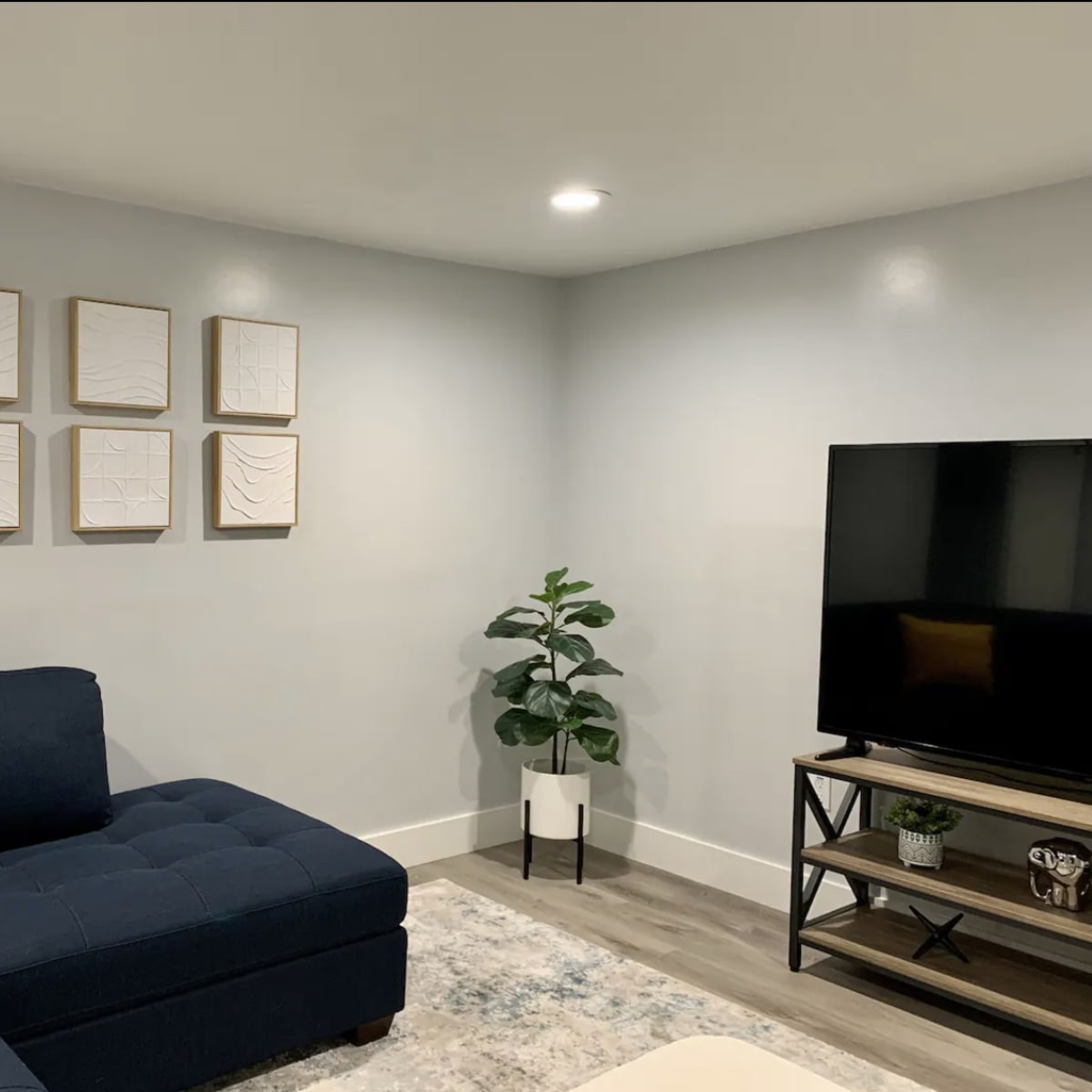 A modern living room with a blue sectional sofa, framed abstract wall art, a television on a stand, and a potted plant in the corner.