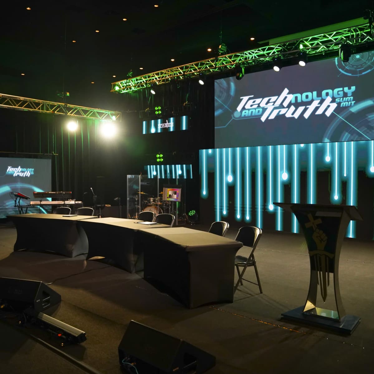 A stage setup for an event titled "Technology and Truth" featuring a podium, table, and screens with lighting effects.