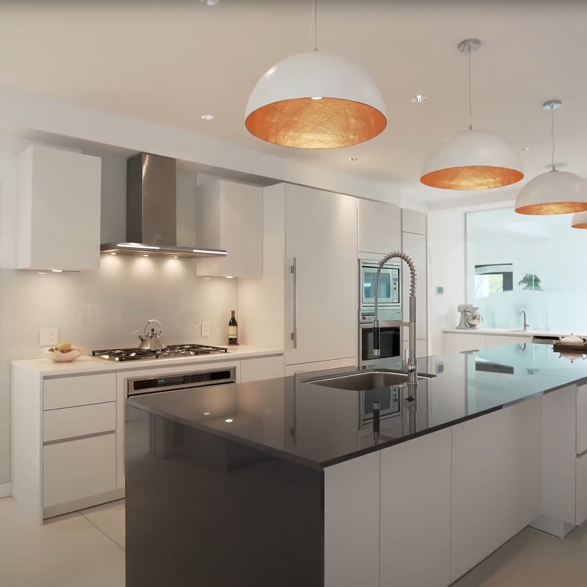 The kitchen features a central island with a dark countertop, modern appliances, and pendant lights above, set against a backdrop of white cabinetry and a large window.