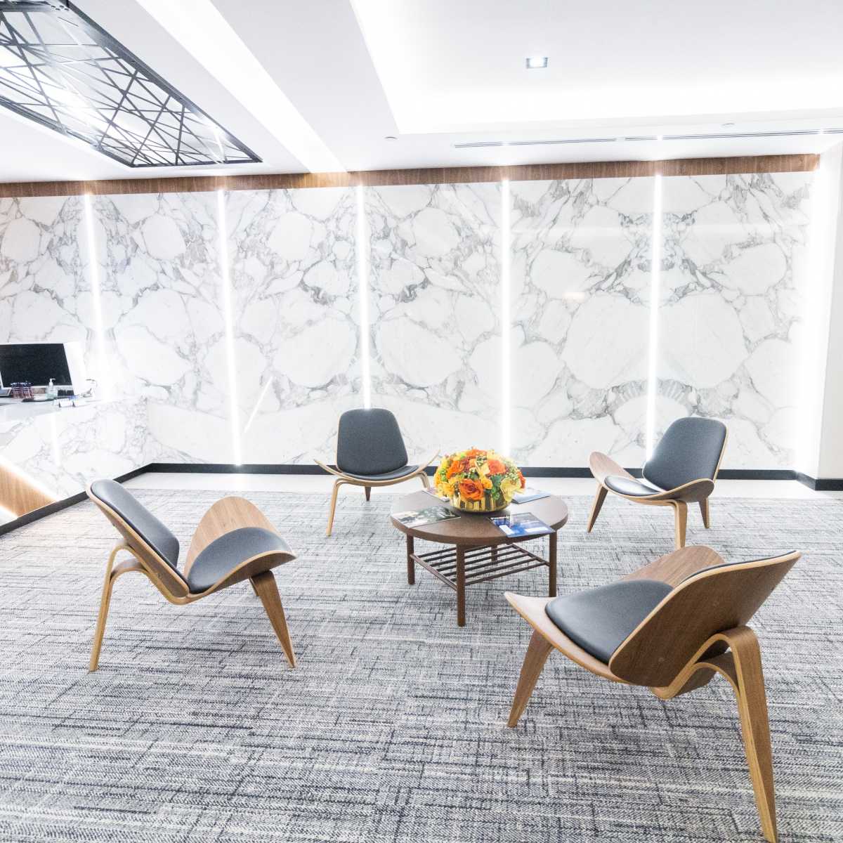 A modern waiting area with four wooden chairs arranged around a central coffee table, set against a marble wall backdrop.