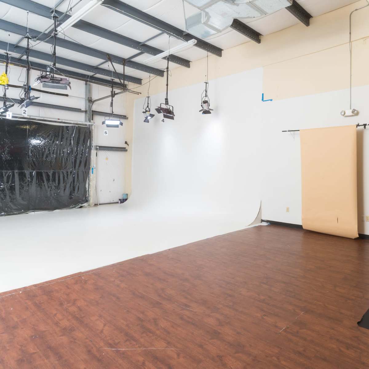 A photography studio with a white backdrop, a brown paper roll, and a dark floor.