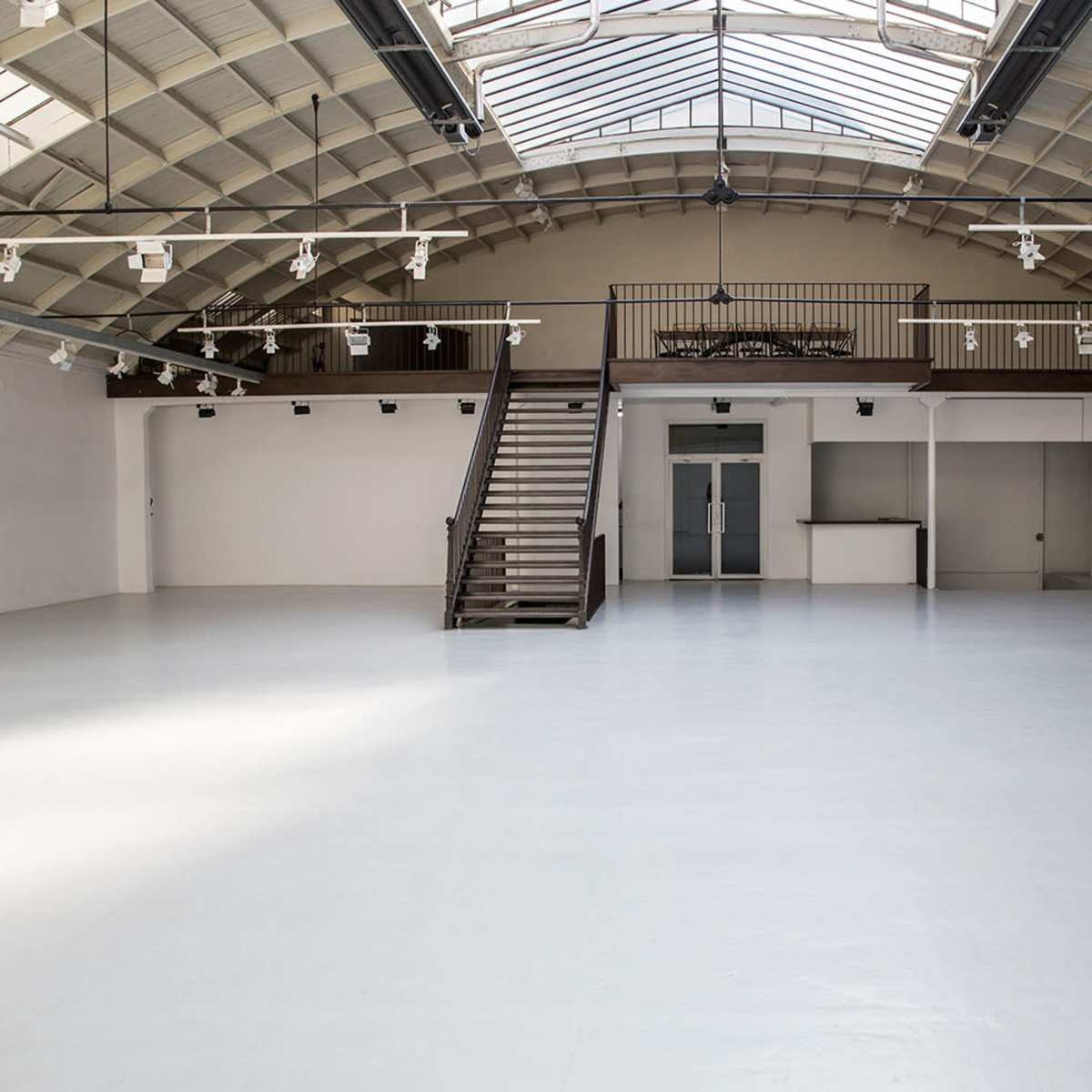 An empty, spacious interior with a high ceiling, large windows, and a staircase leading to a balcony.