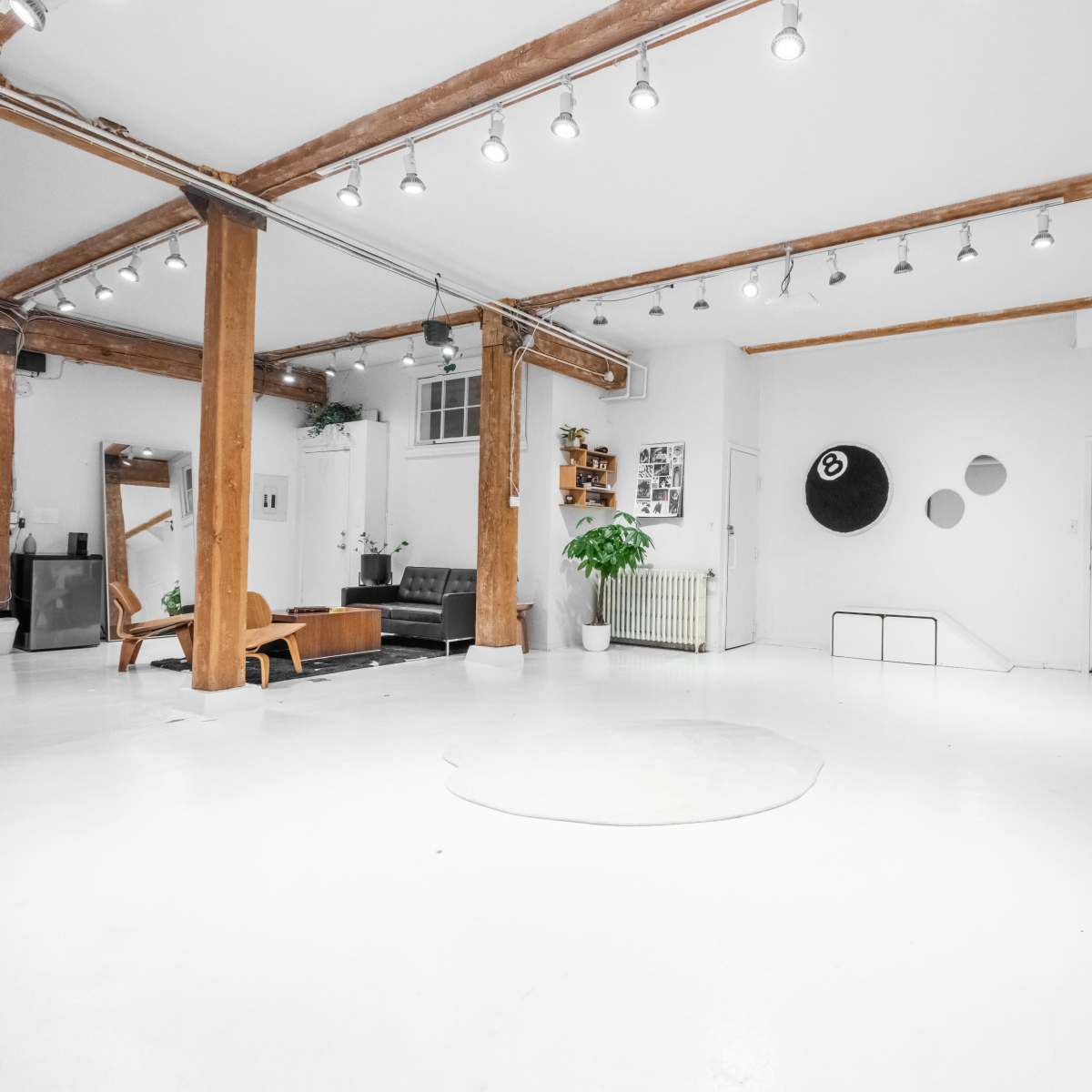 A spacious, minimalist room with exposed wooden beams, white walls, a black leather sofa, and contemporary furniture.