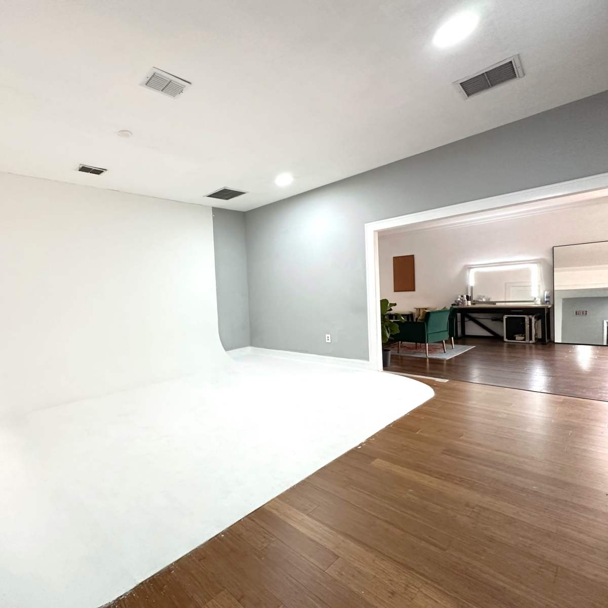 A spacious, minimalist photo studio with a curved white backdrop and hardwood flooring.