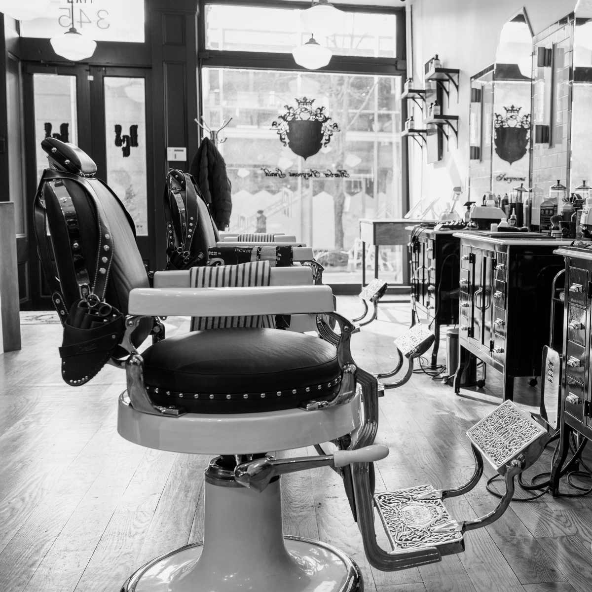 An empty barbershop with vintage barber chairs and salon equipment arranged around a polished wooden floor.