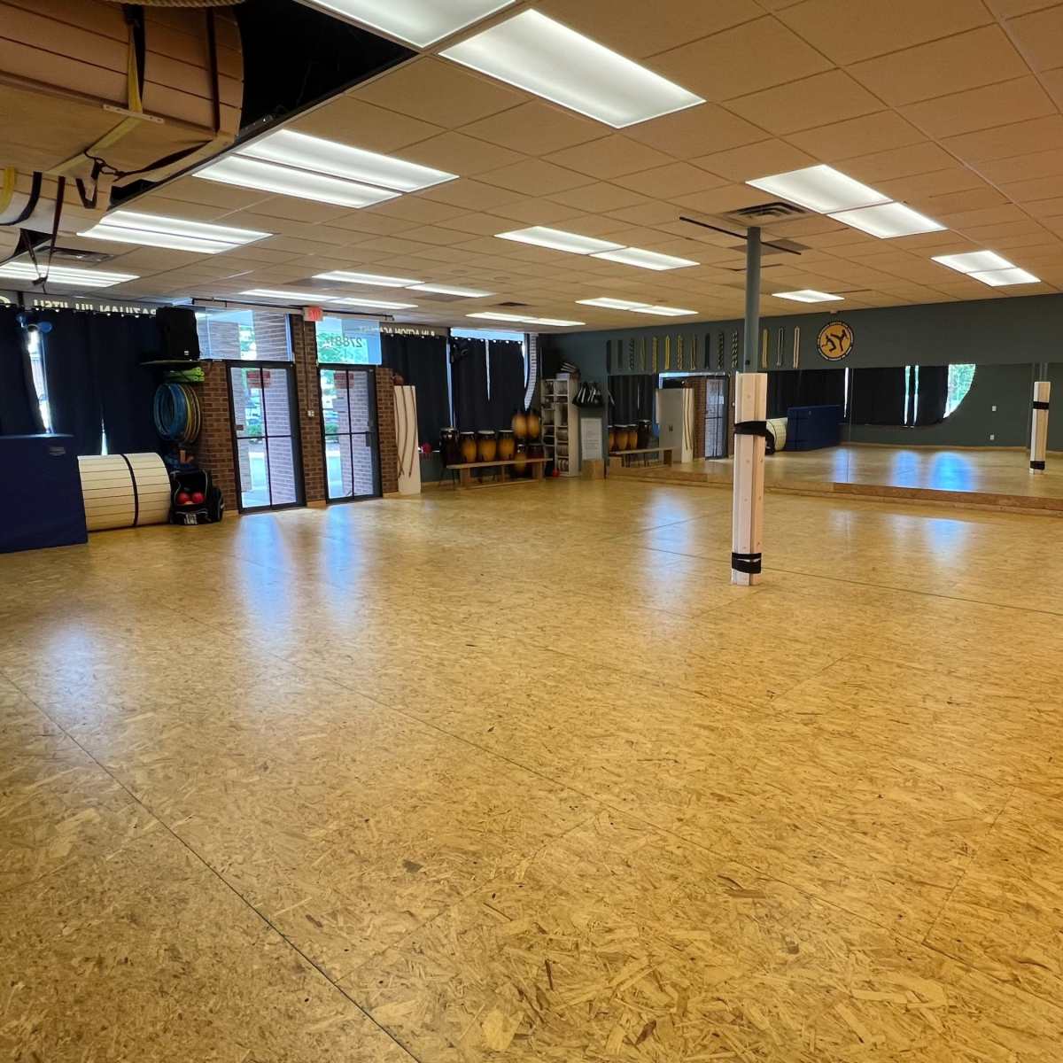 An empty fitness studio with wooden flooring, mirrors, and exercise equipment along the walls.