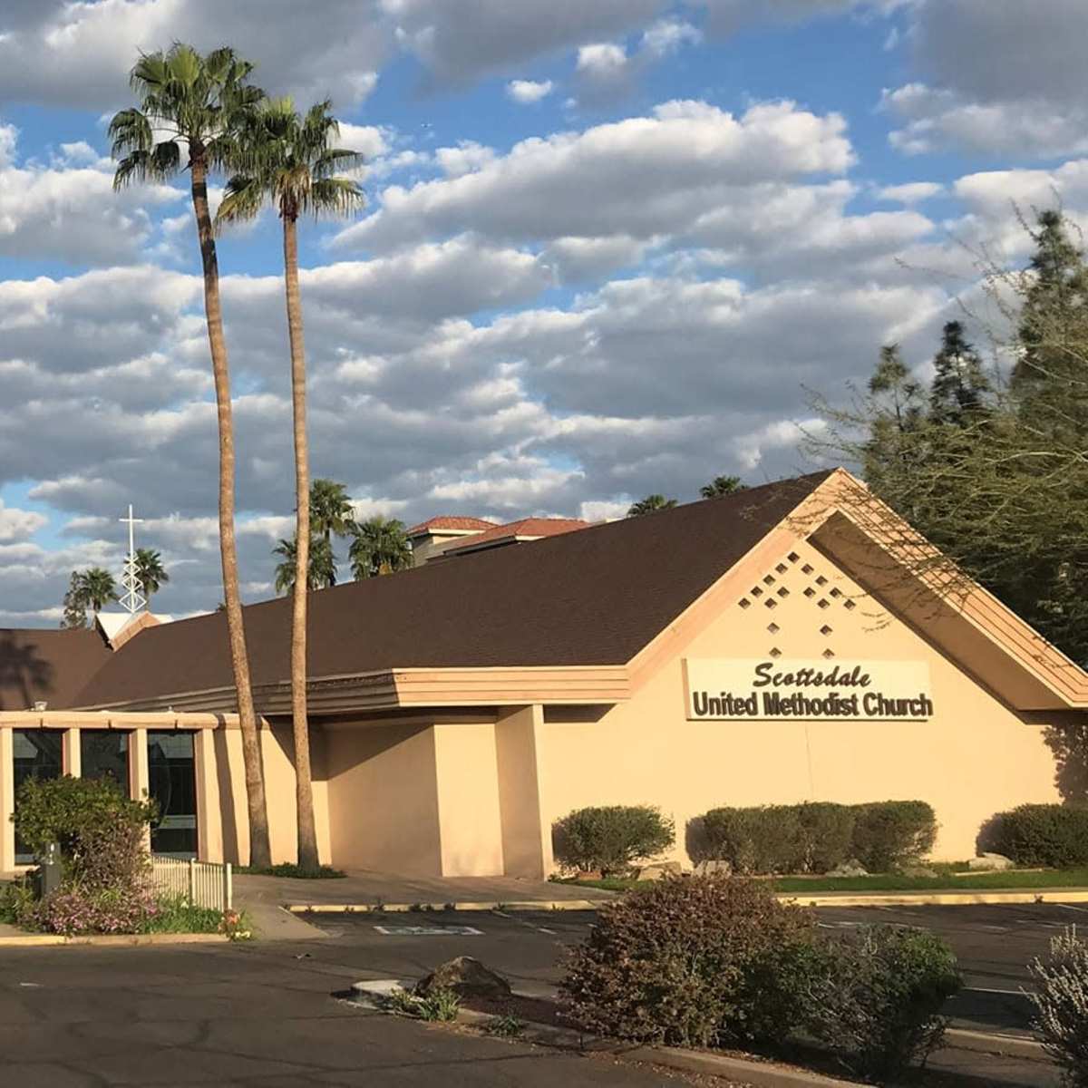 Scottsdale United Methodist Church, featuring a tall spire and palm trees under a partly cloudy sky.