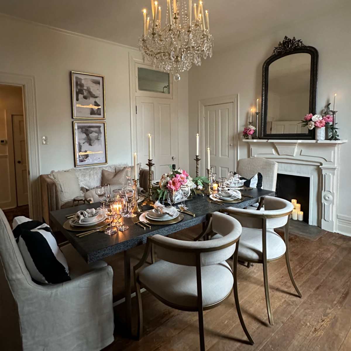A beautifully set dining table is positioned in a well-decorated room featuring a chandelier, a fireplace, and floral arrangements.