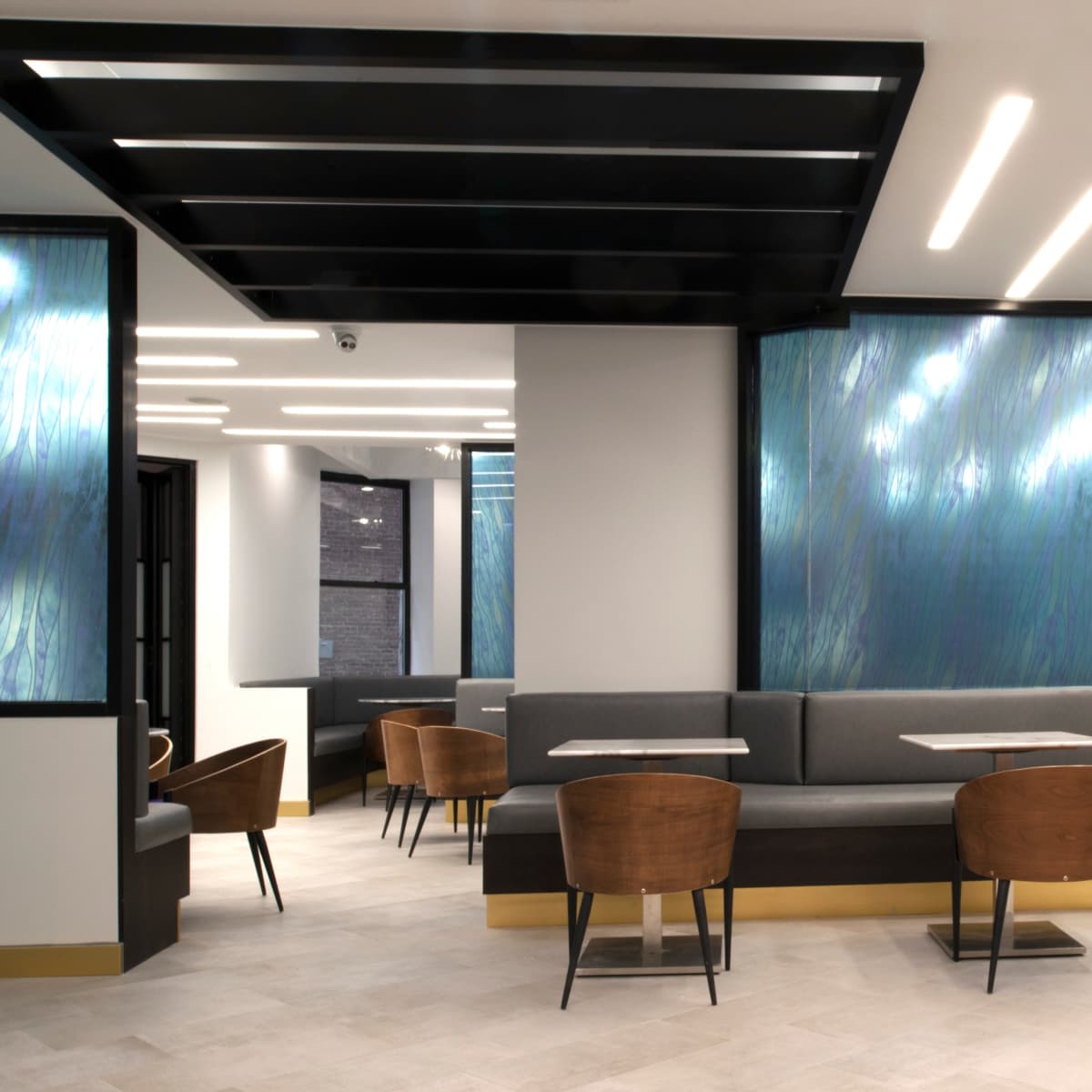 A modern café interior with seating areas featuring wooden chairs and tables, illuminated by sleek ceiling lights and decorated with blue-toned wall panels.