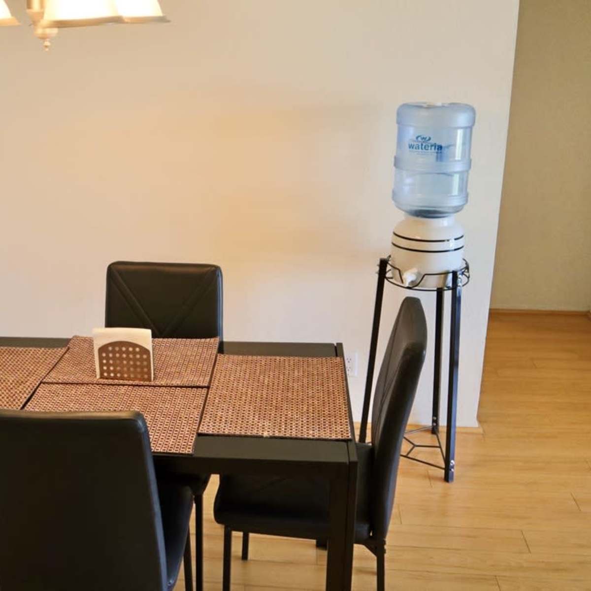 A black dining table with four chairs is set in a room, accompanied by a water cooler positioned on a stand.