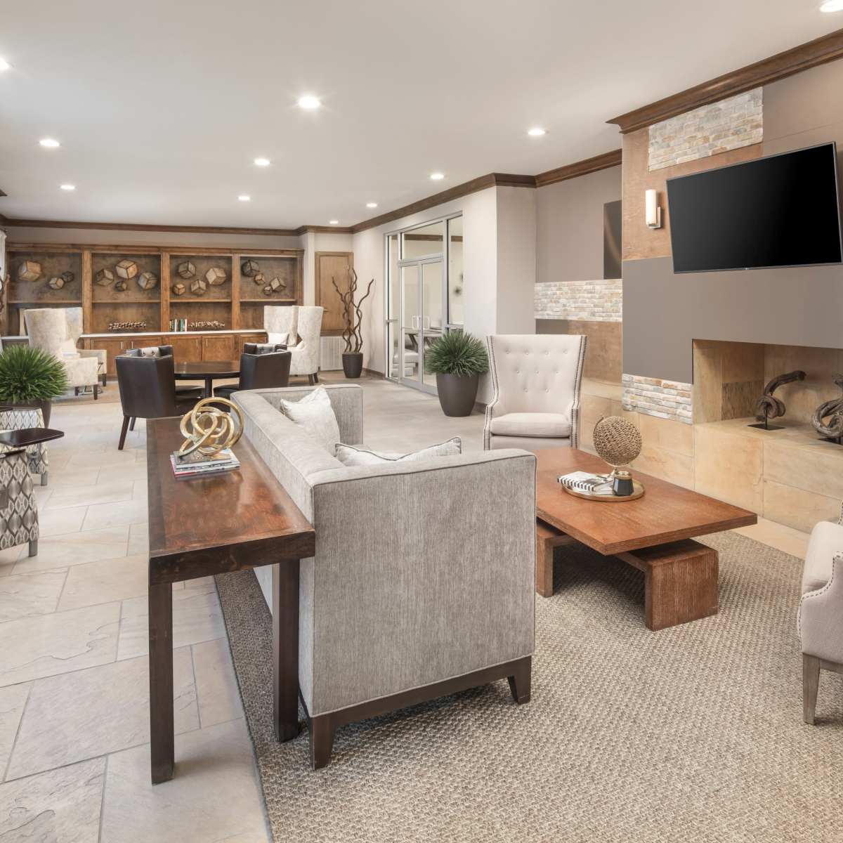 A modern living room with a cozy seating arrangement, a wooden coffee table, and a stone fireplace, complemented by large windows and wooden cabinetry.