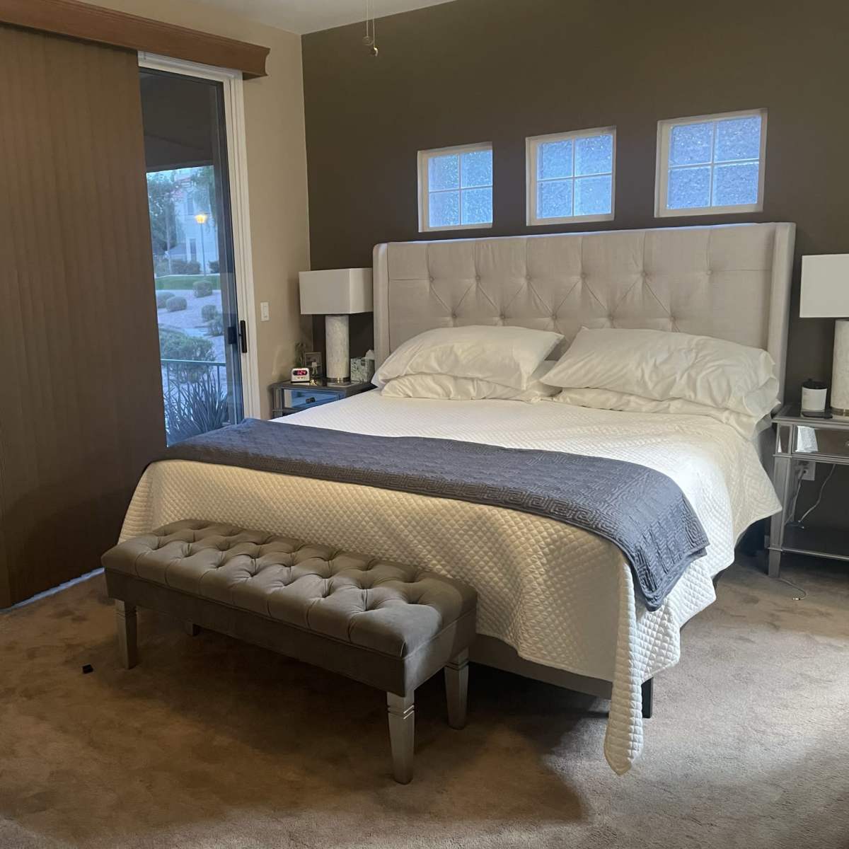 A bedroom with a bed, a bench at the foot, and sliding glass doors leading to an outdoor area.