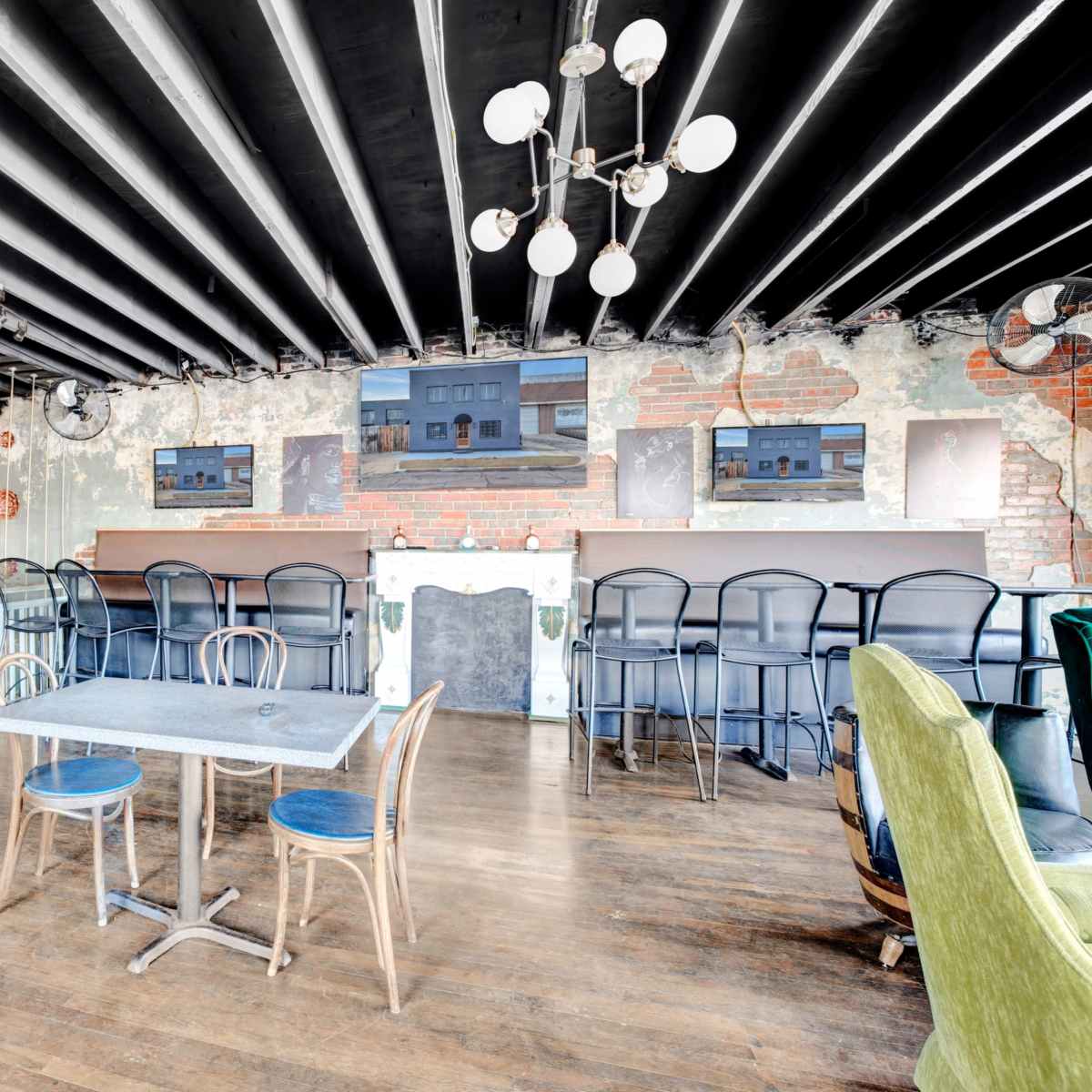An interior space with a mix of exposed brick walls and wooden flooring, featuring a table and chairs, along with a bar area in the background.