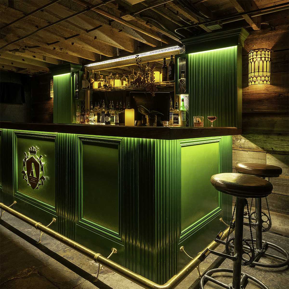 A green bar illuminated with soft lighting, accompanied by several high stools.