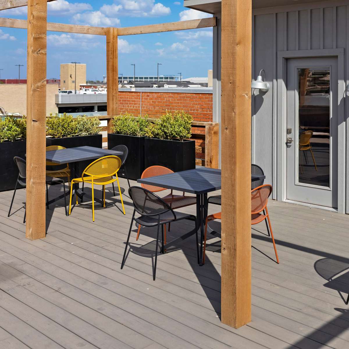 A rooftop patio with colorful chairs and tables arranged around planters and a door leading inside.