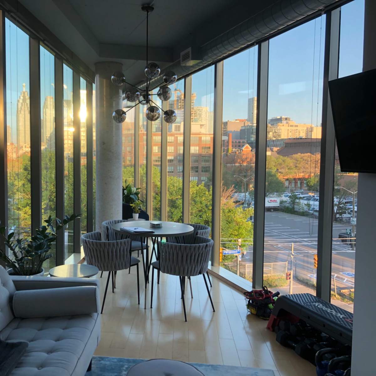 A modern living space features a sitting area with a couch and a dining table surrounded by large windows showcasing a city skyline.