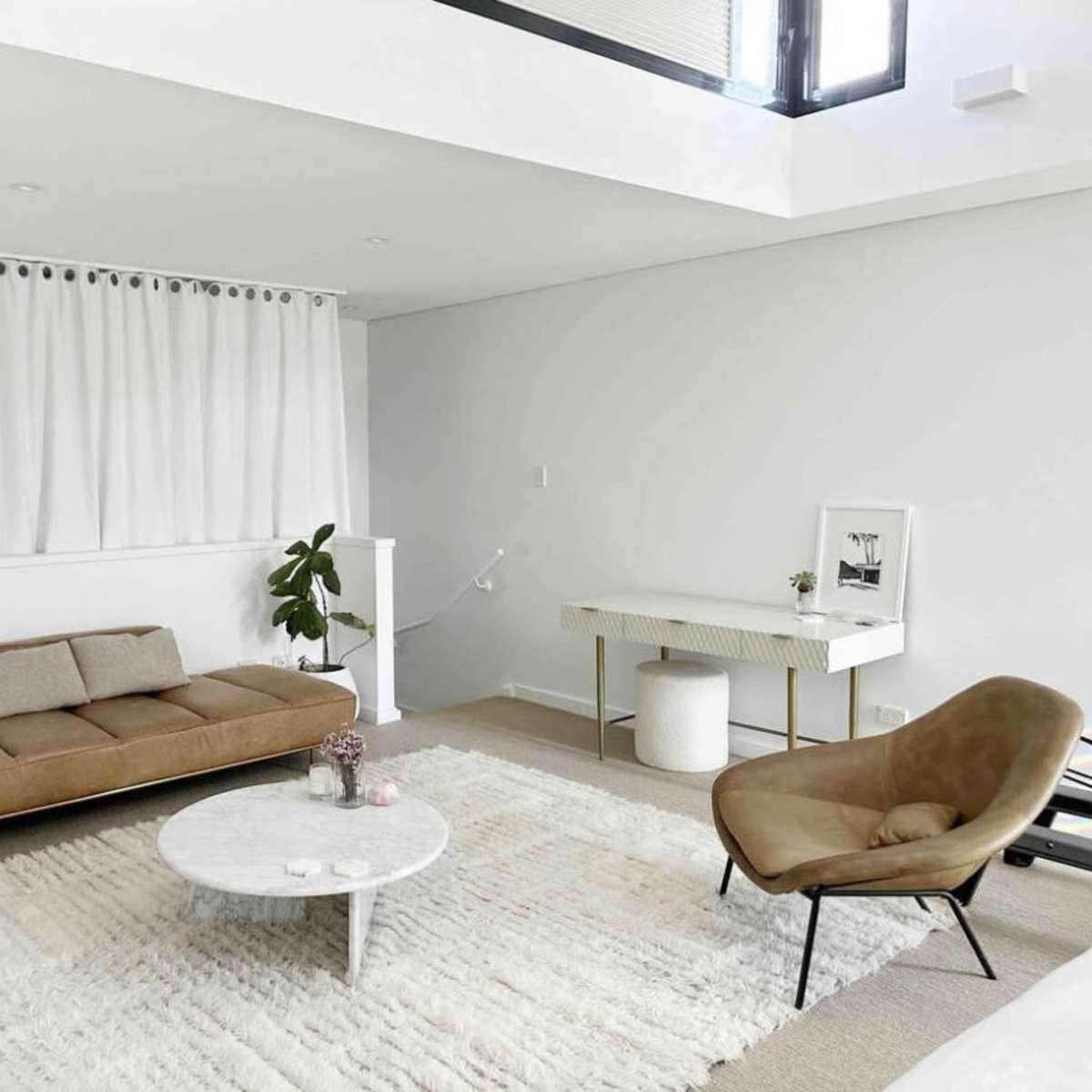 A bright, modern living room featuring a brown sofa, a round coffee table, a chair, and a white rug on the floor.