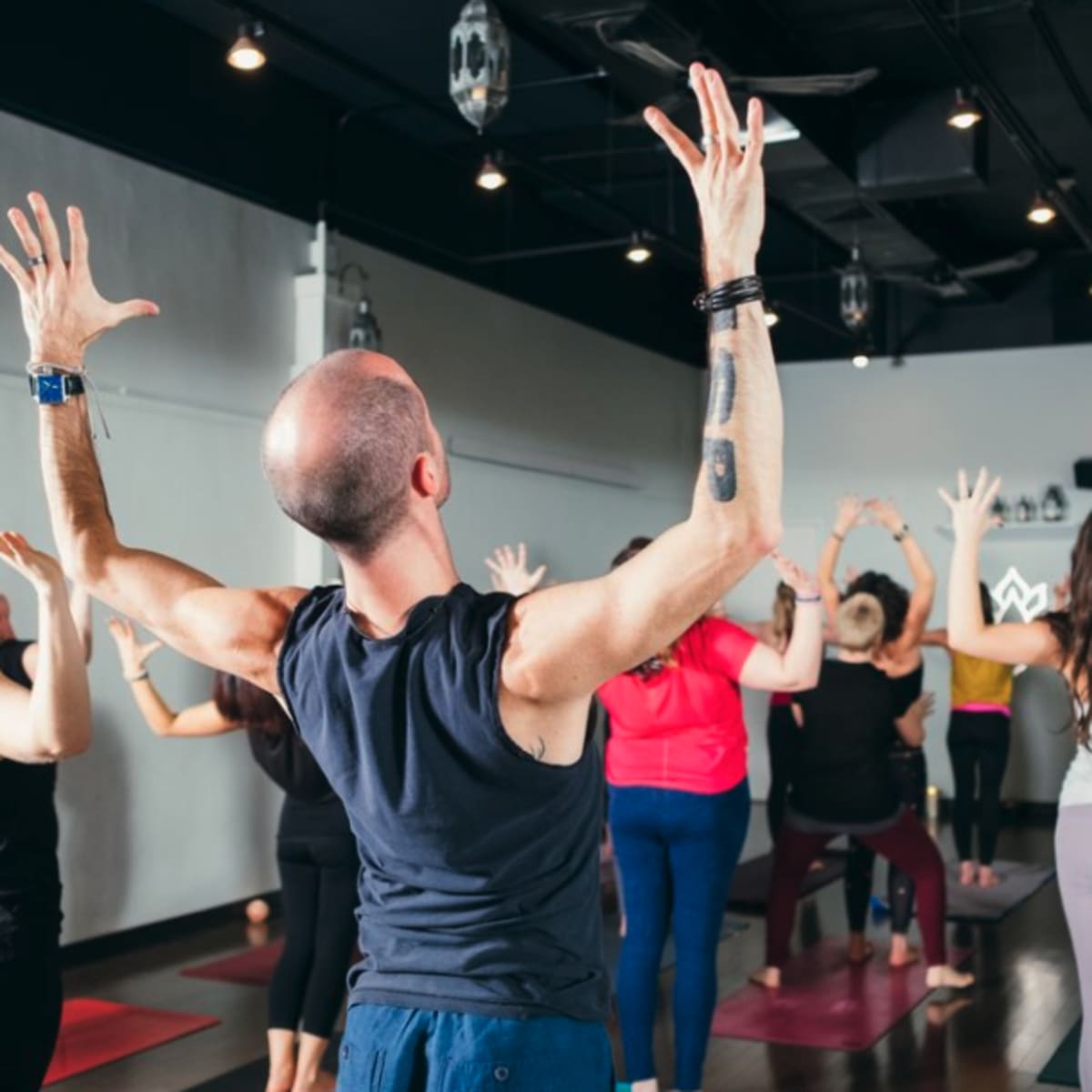 A group of people is participating in a yoga class, with various individuals positioned in different poses and raising their arms.