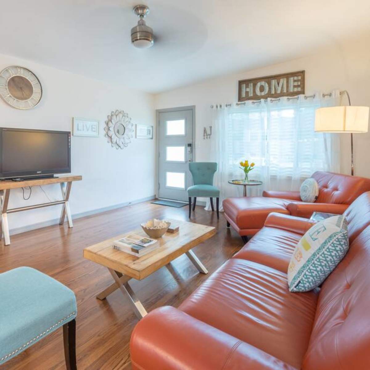 A cozy living room with a television, two orange sofas, a wooden coffee table, and a light blue chair, all arranged around a door with a window.