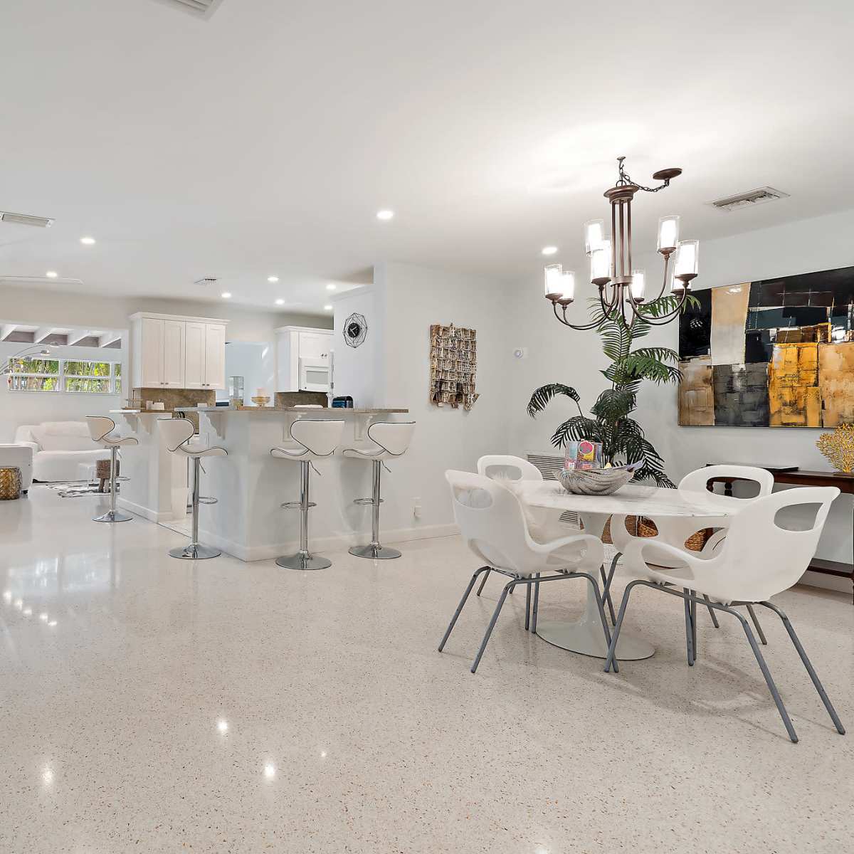 A modern open-concept living area with a white kitchen, bar seating, and a dining table.