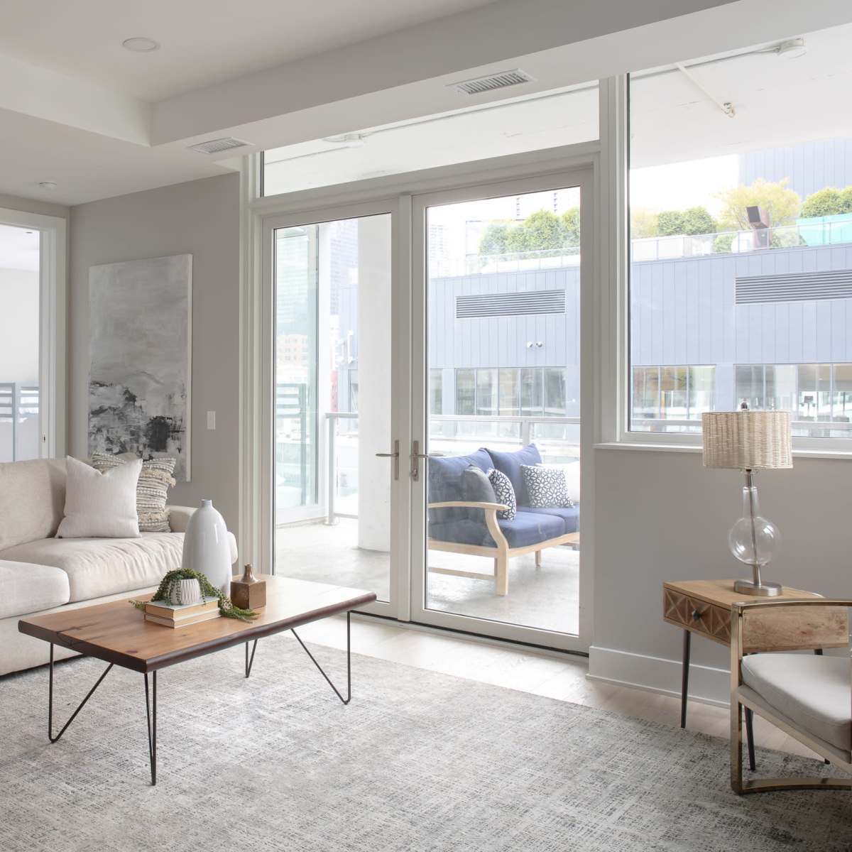 A modern living room with a beige sofa, a wooden coffee table, and large windows providing natural light.