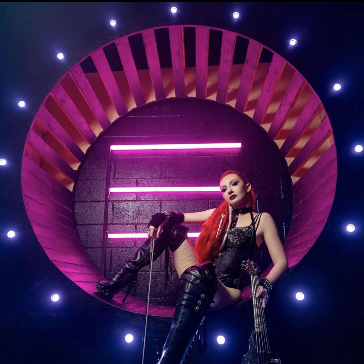 A figure poses with a guitar in a dramatic circular backdrop illuminated by bright lights.