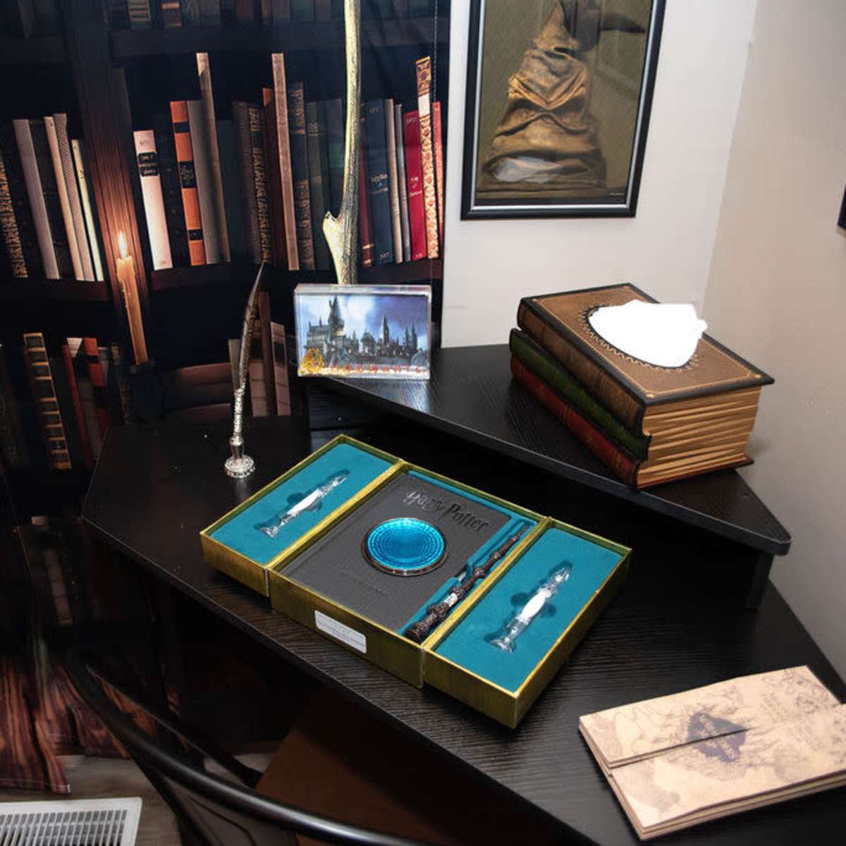 A dark wooden desk with a collection of decorative items, including a box set of "Harry Potter" memorabilia, quills, and a framed photo, all set against a backdrop of bookshelves filled with books.