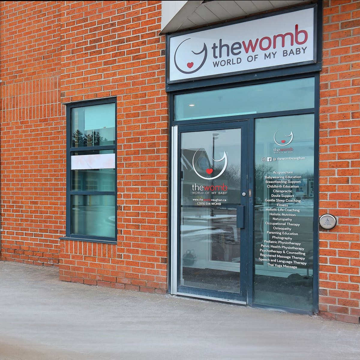 The entrance of a brick building featuring glass doors with the logo and name of a business called "thewomb" on the window.