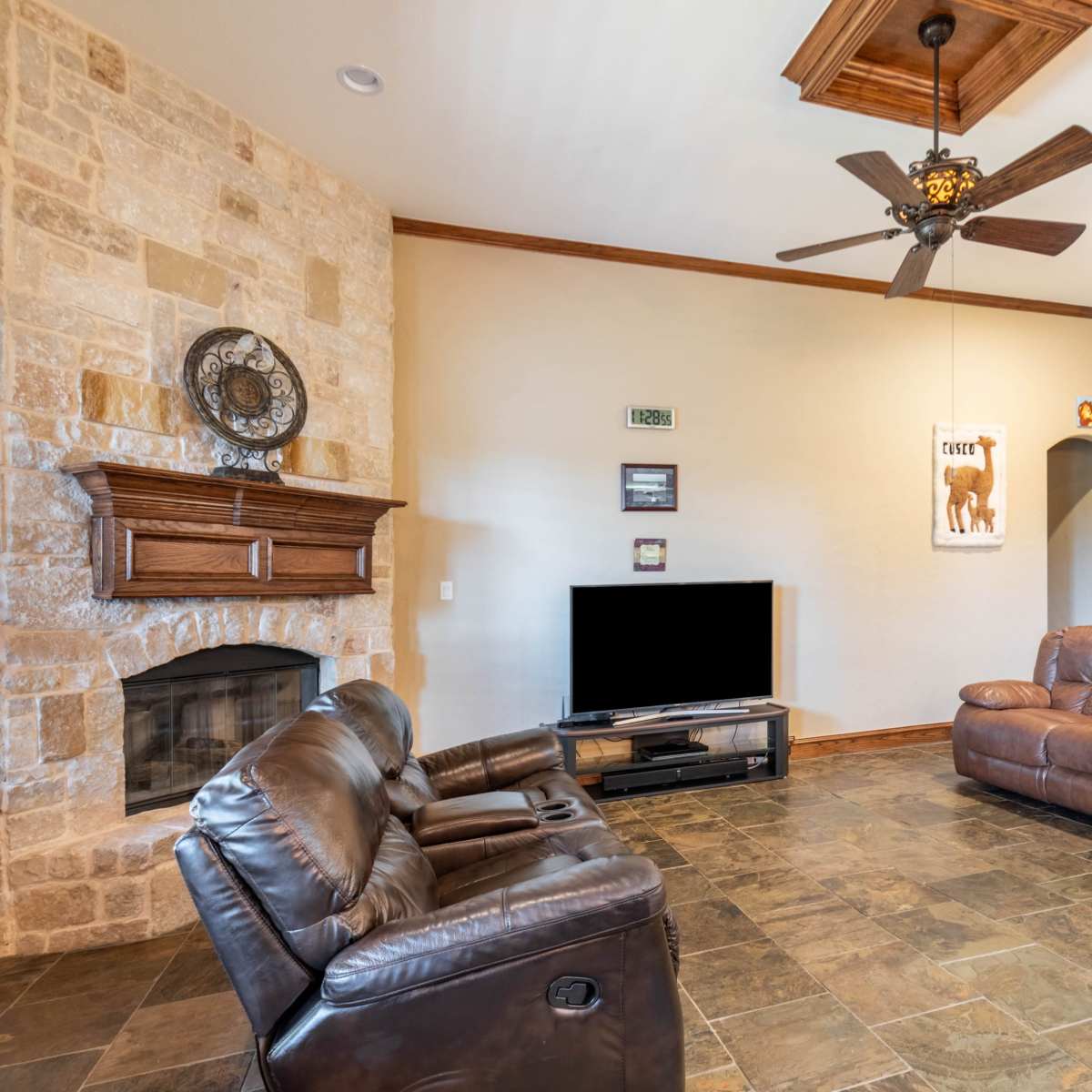 The living room features a stone fireplace, two leather sofas, and a television on a stand against a wall with wooden trim.