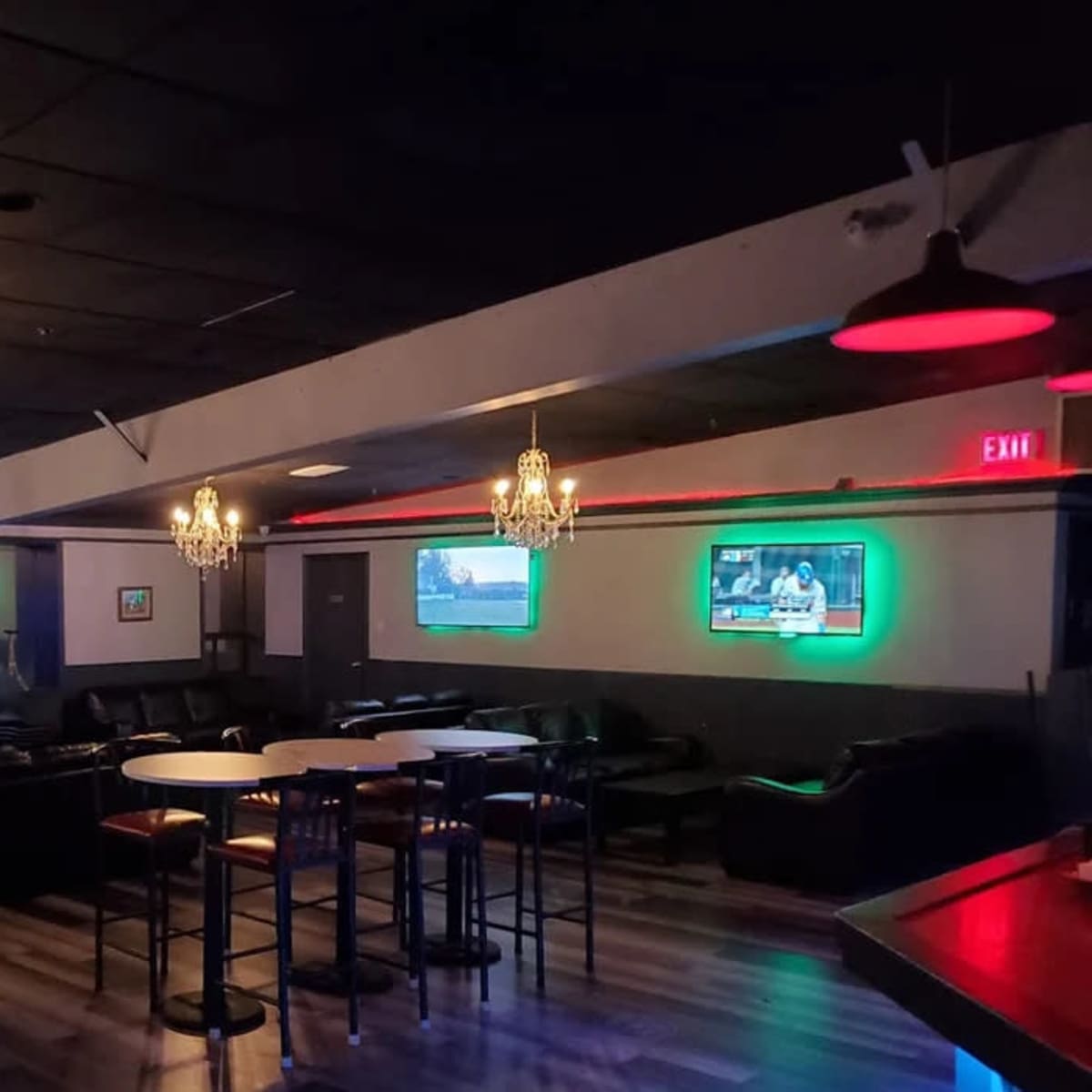 A dimly lit lounge area with leather couches, several televisions displaying sports broadcasts, and decorative chandeliers.