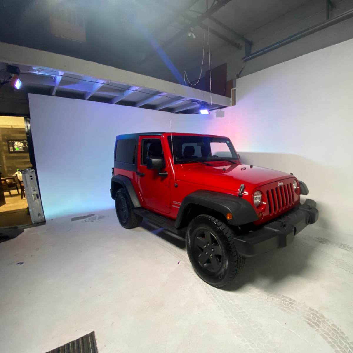 A red Jeep Wrangler is parked in a photo studio with a plain white backdrop.