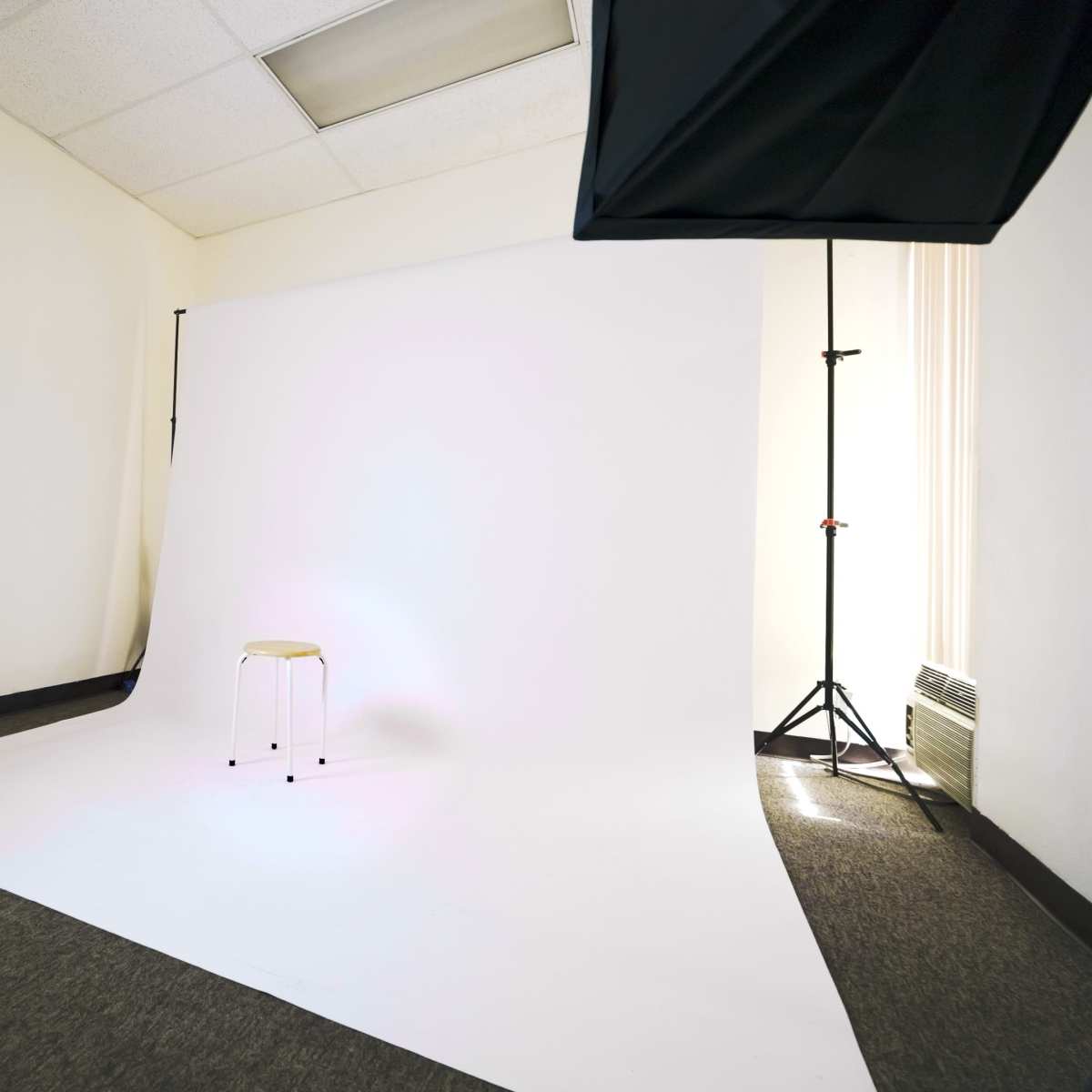 A photography studio with a white backdrop, a stool in the center, and professional lighting equipment set up.