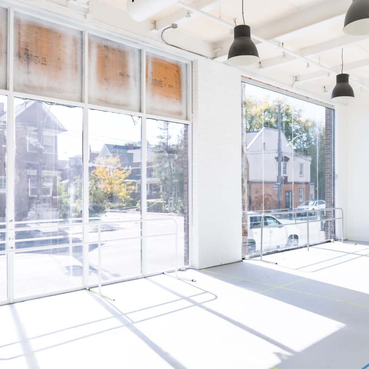 A spacious, well-lit studio with large windows, wooden floors, and ballet barres positioned against the walls.