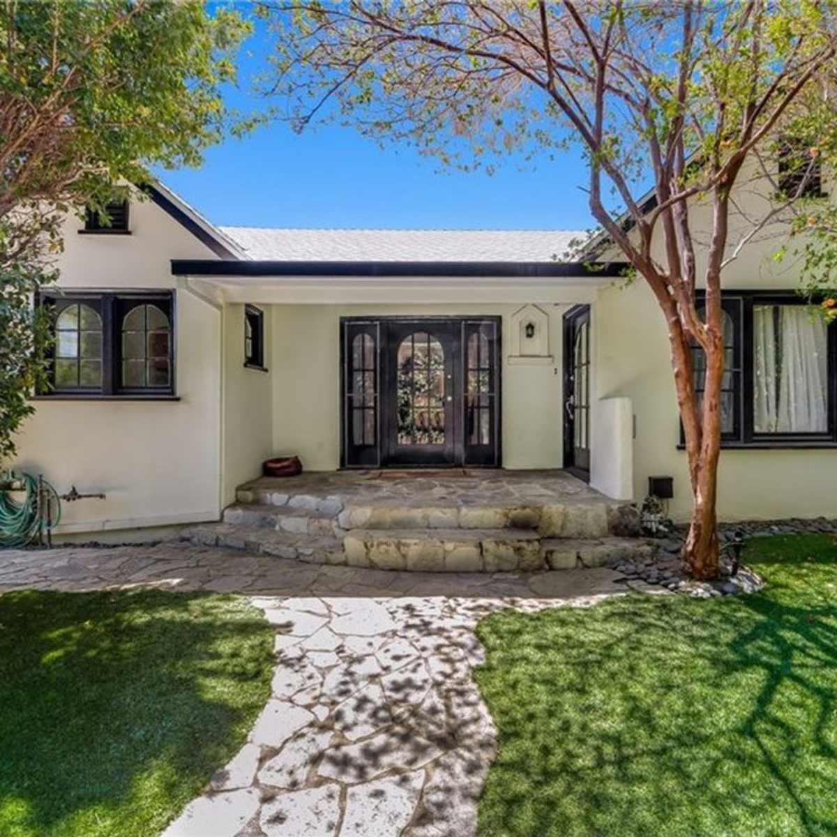 A charming white house with a stone pathway leading to a front entrance, surrounded by green grass and trees.