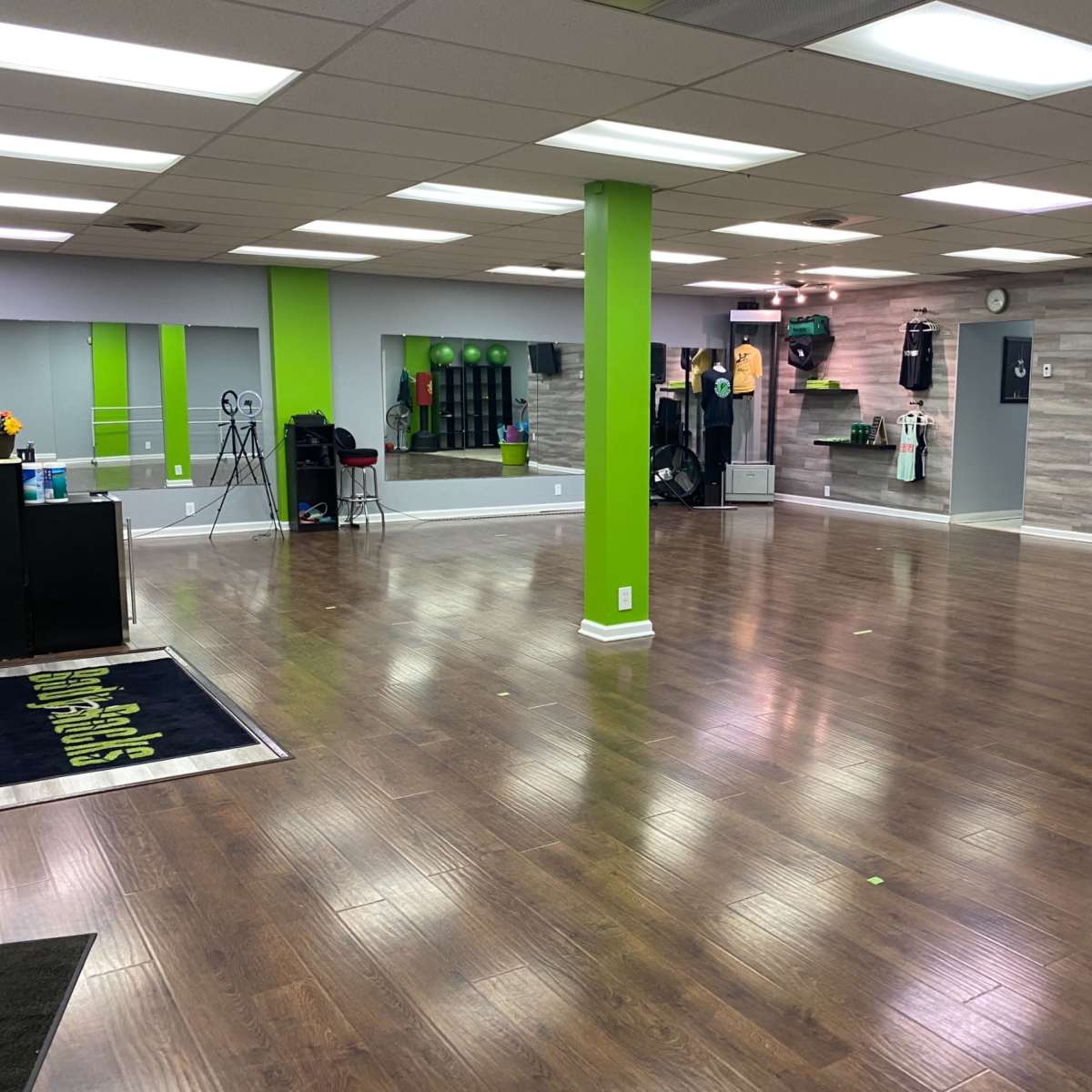 A spacious indoor gym with wooden flooring, green accent walls, and various fitness equipment arranged along the sides.