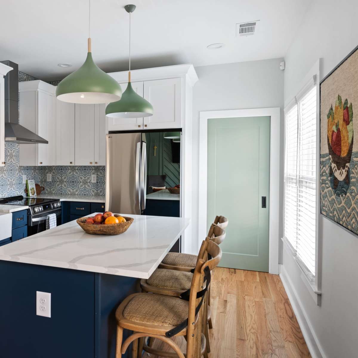 A modern kitchen features white cabinetry, a blue island with seating, and decorative tile backsplash.