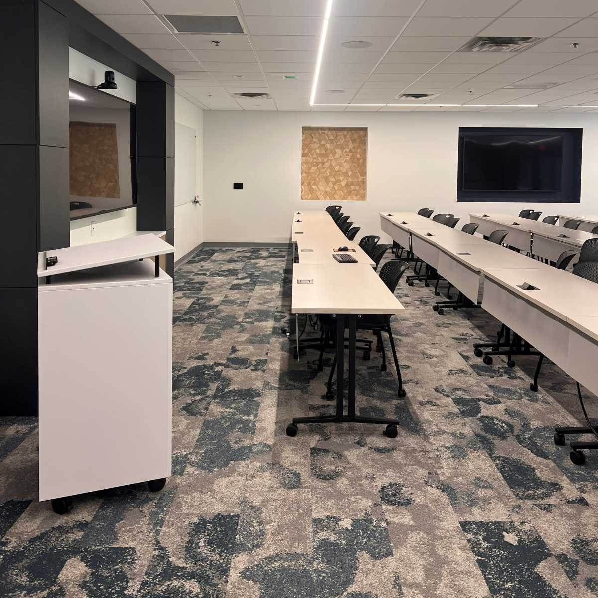 A modern conference room with rows of tables and chairs, featuring a podium and large displays on opposite walls.
