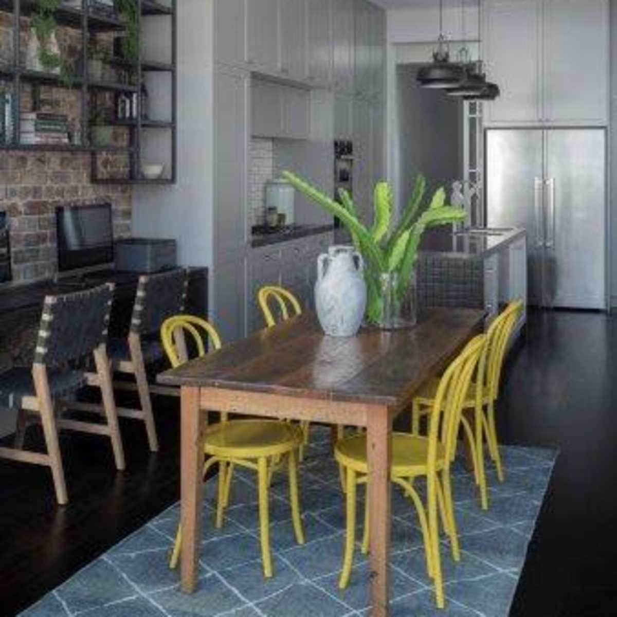 A modern kitchen and dining area with a wooden table surrounded by yellow chairs, a brick wall feature, and sleek cabinetry.