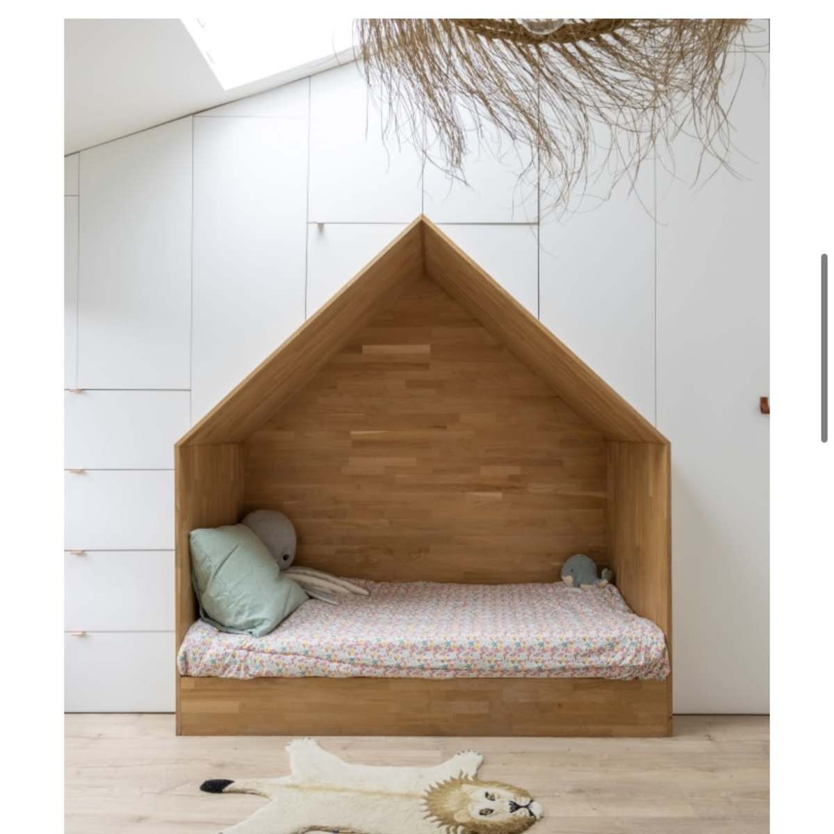 A wooden bed designed like a house, located against a white wall with storage drawers.