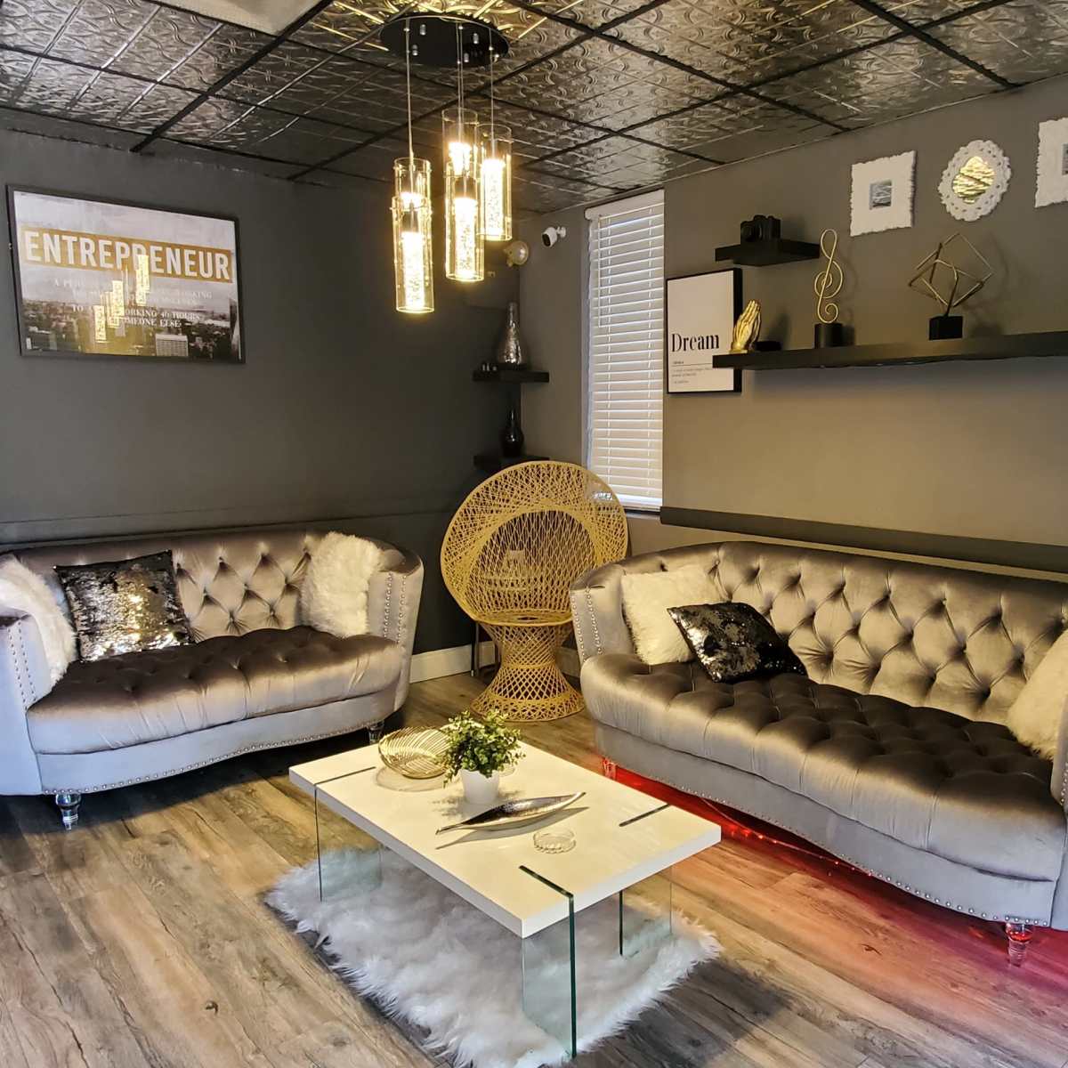 A modern office interior featuring two tufted sofas, a glass coffee table, a decorative chair, and wall art with motivational themes.
