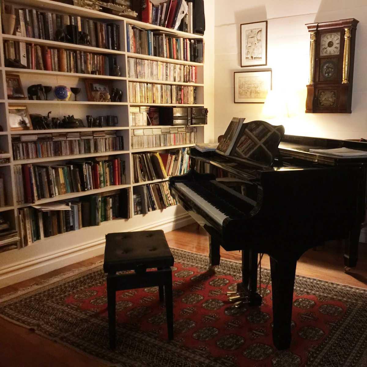 A grand piano sits next to a bookshelf filled with books, and a tall clock stands in the background of a cozy room.