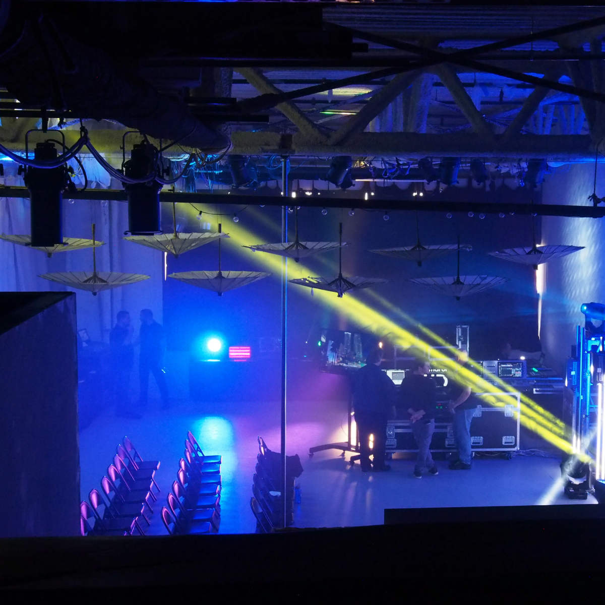 A spacious event venue with rows of empty chairs and colorful stage lighting being set up for an upcoming performance.