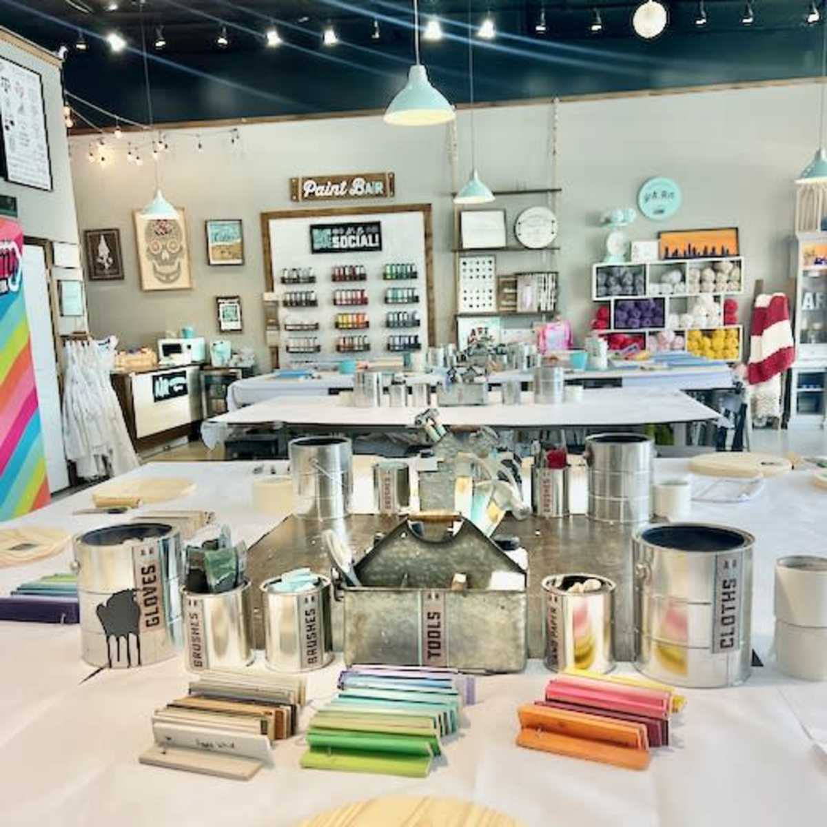 A craft studio with tables set up for painting, surrounded by paint supplies, tools, and decorations on the walls.